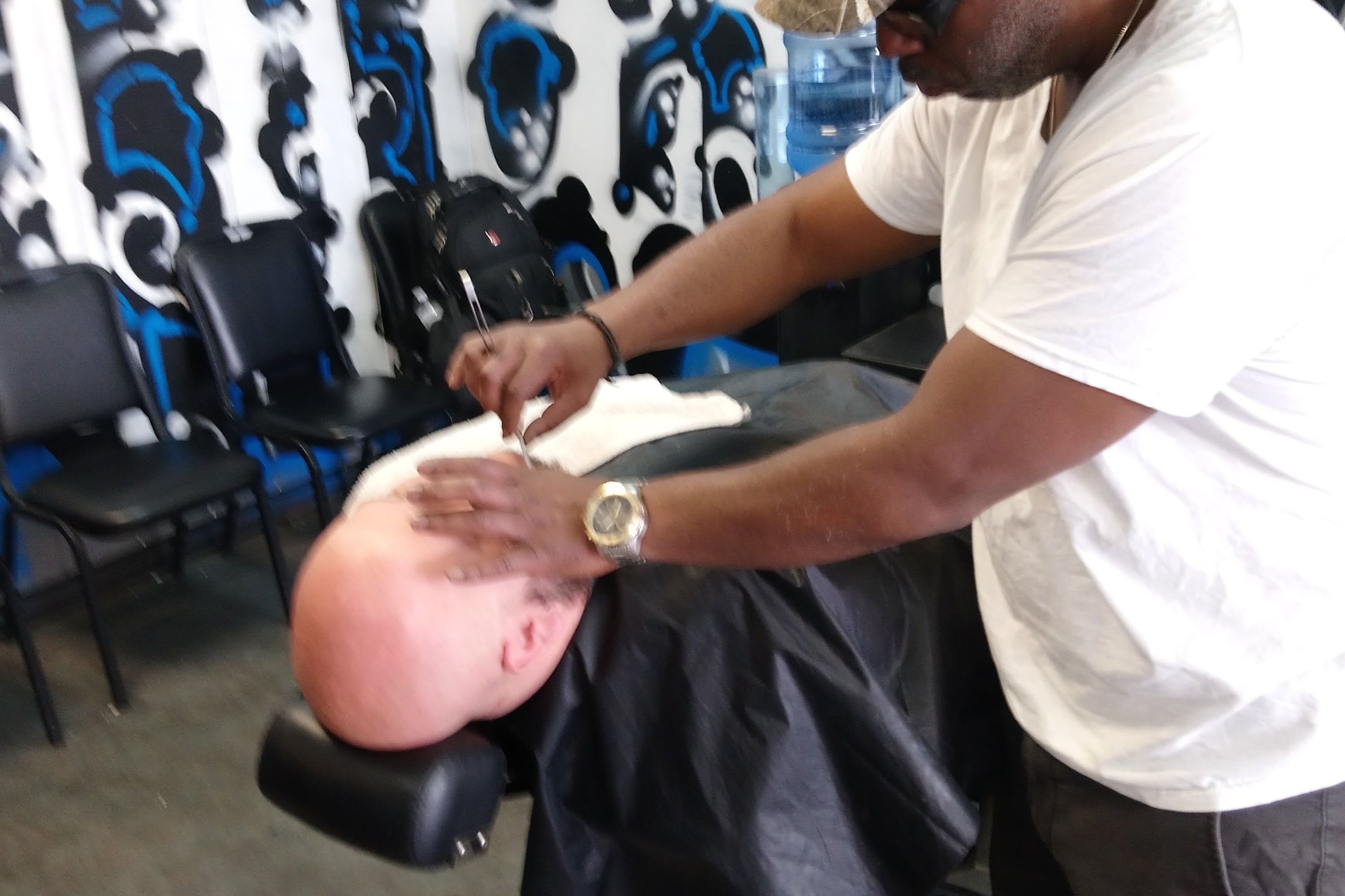 The shop: a barber chair, a straight razor in hand, waiting chairs and a painted wall